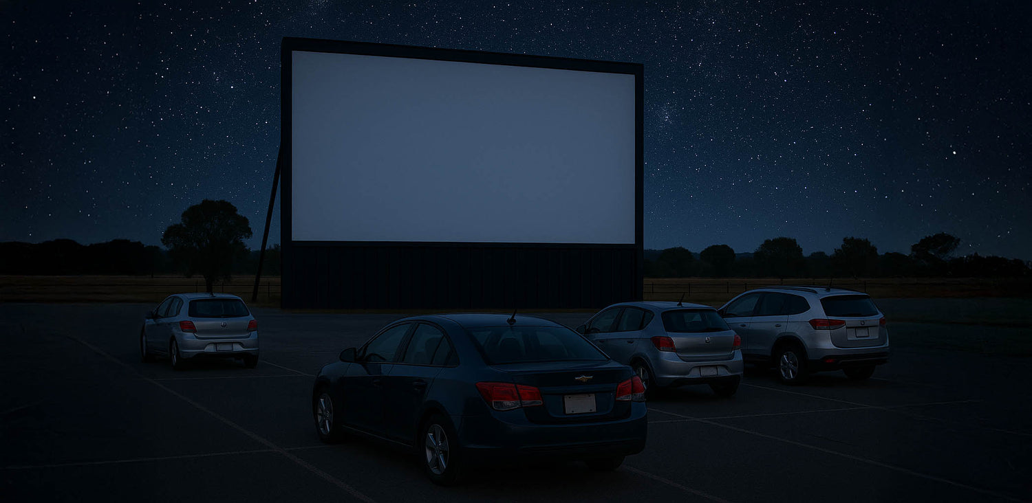 Drive-in theater with cars parked under a large screen at night.