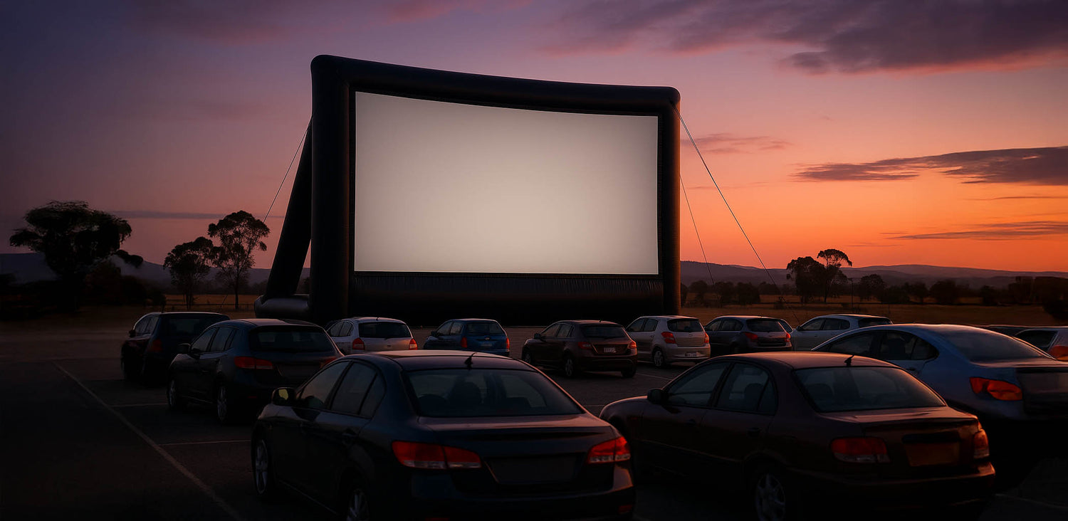 Drive-in style Inflatable movie screen set up in a parking lot with cars at sunset.