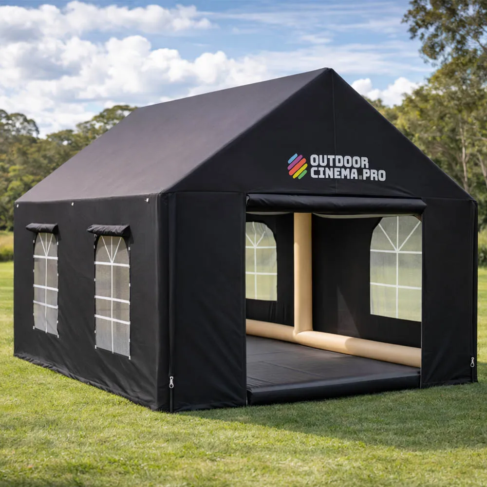 A black Outdoor Cinema Pro branded inflatable tent with windows and an open front, set up on grass