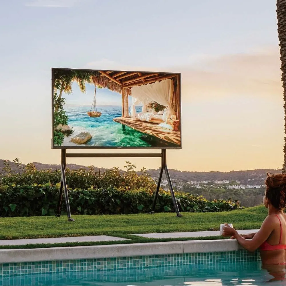 A weatherproof outdoor television mounted on a stand beside a swimming pool in bright daylight