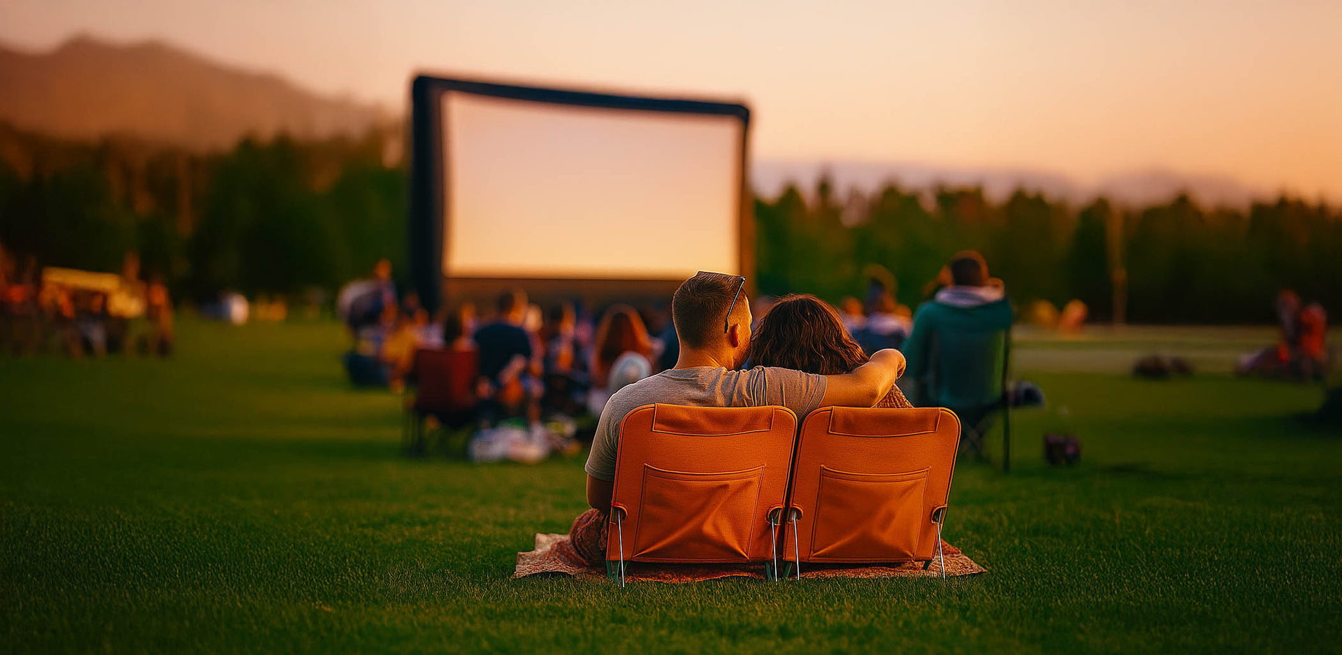 People watching a large inflatable movie screen in a park at sunset.