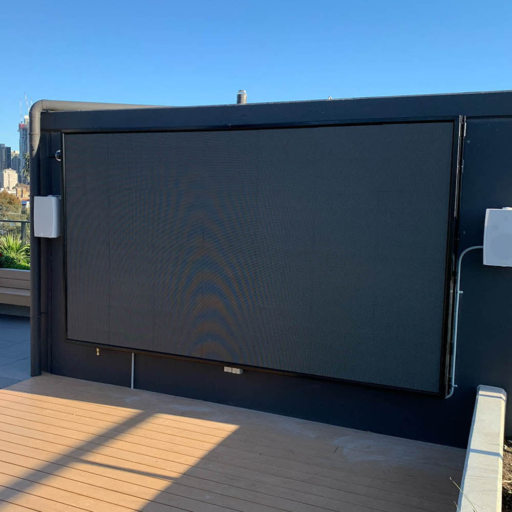 Large outdoor LED screen mounted on a rooftop with speakers mounted to the wall with city skyline in the background