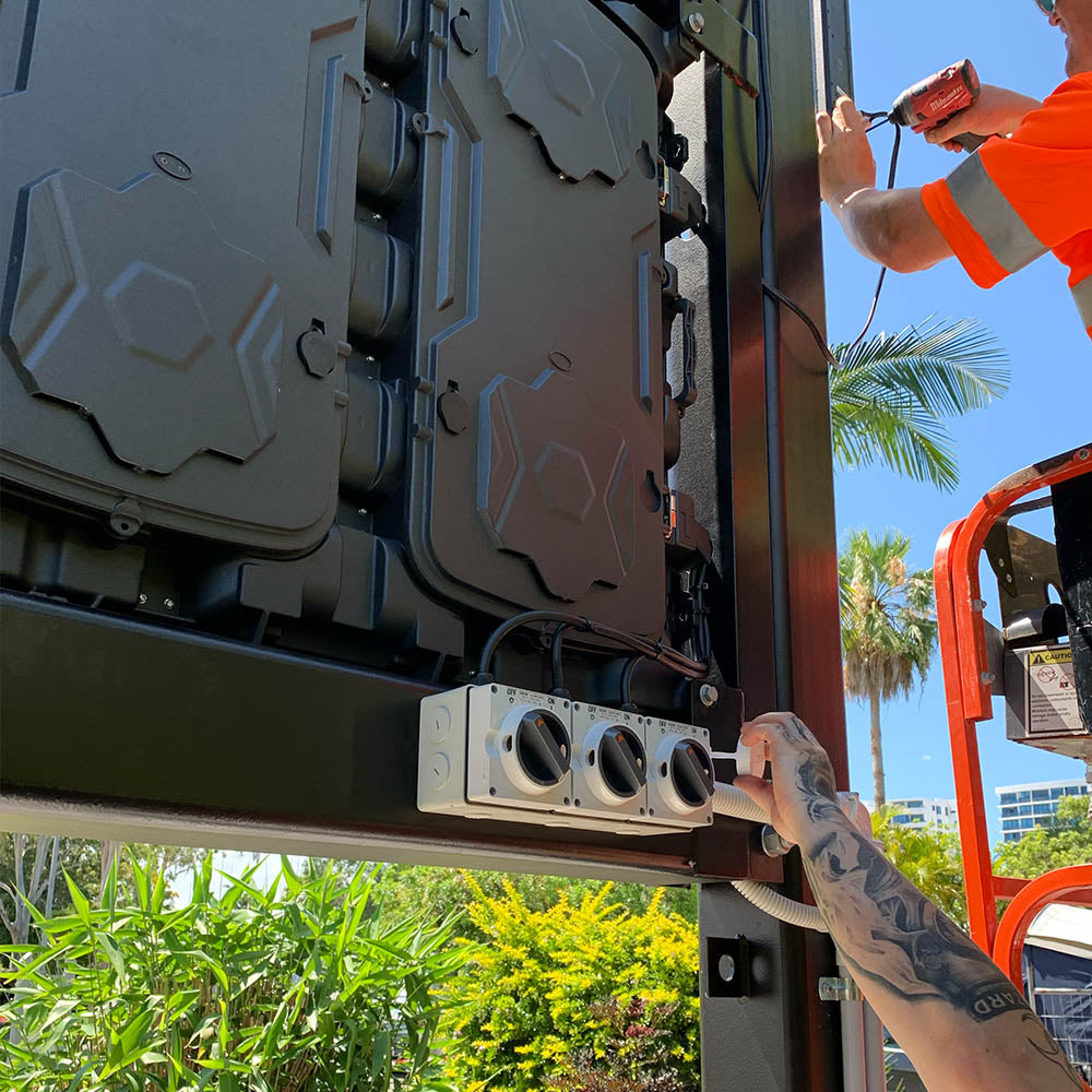 Person working on the rear of a large LED display cabinet within a steel frame.