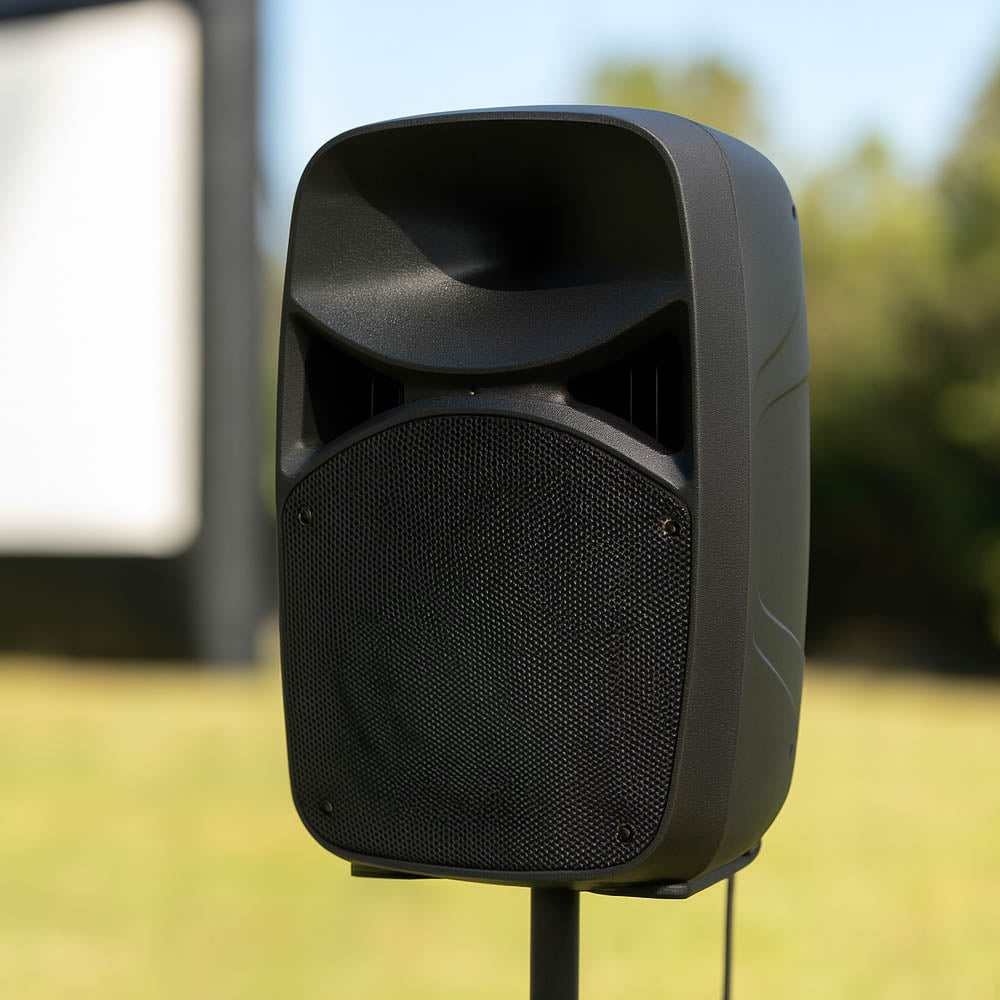 Black outdoor speaker on a stand with a blurred natural background and cinema screen