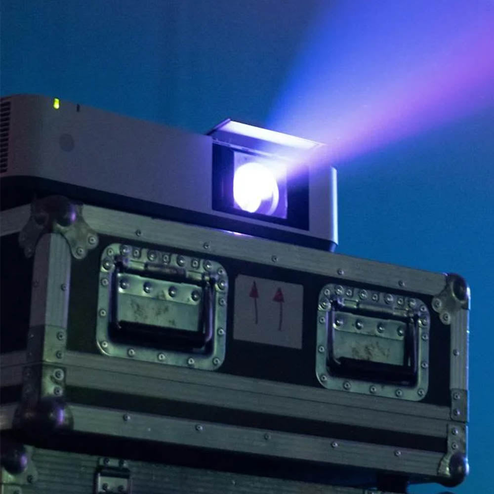 Large venue projector on top of equipment with a purple beam against a dark background in a theatre
